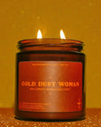 Gold Dust Woman Candle by Faire with two glowing flames, set against a shimmering gold backdrop.