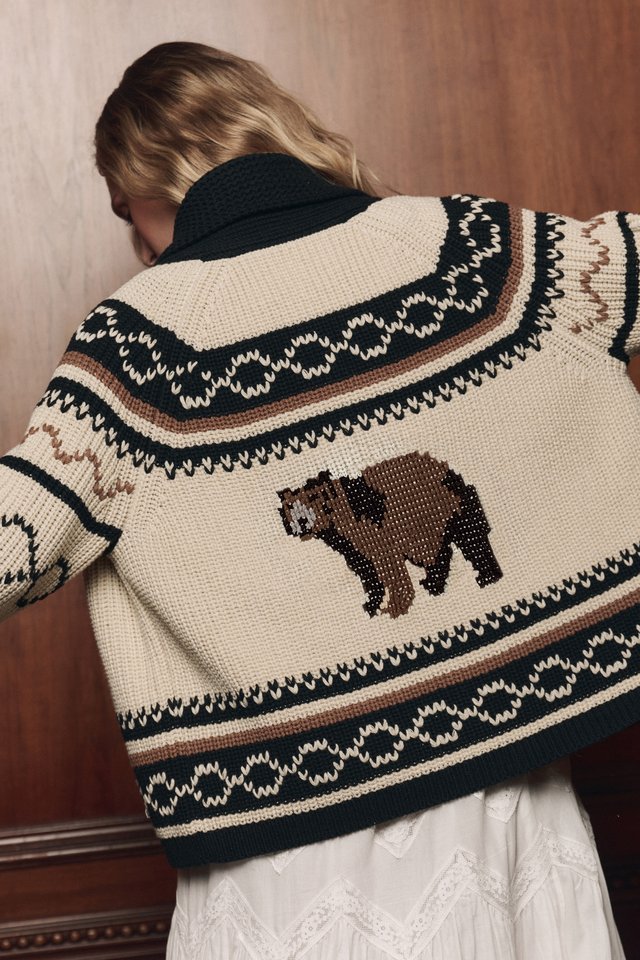 Back of a cream and dark patterned cardigan with a bear motif, worn over a white textured skirt.