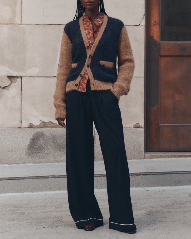 Model in a navy and tan cardigan, red floral shirt and wide navy trousers beside a stone building.