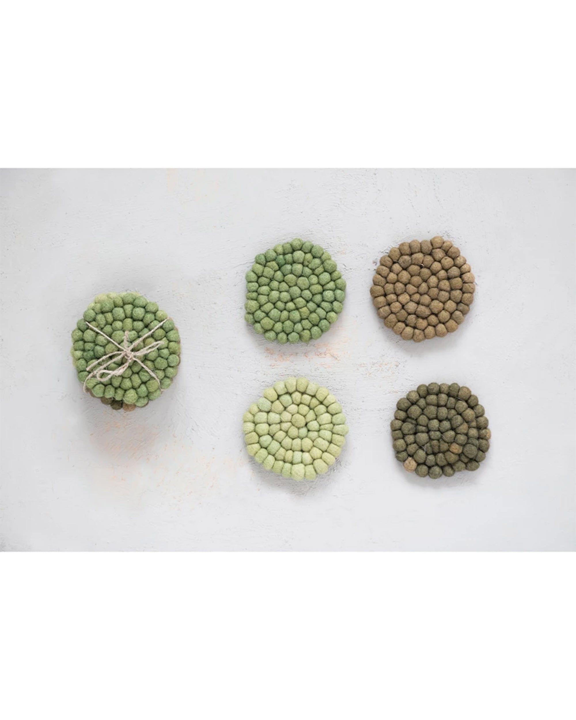 The Creative Co-op Wool Felt Coasters Green Tone S/4 set features four handmade wool felt ball coasters in green and brown hues, beautifully arranged on a light surface—ideal for stylish home décor.