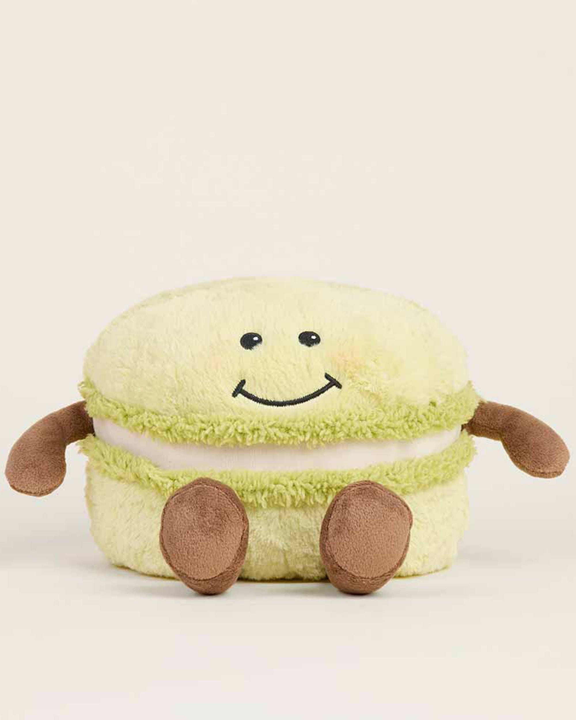 The Faire Green Macaroon Warmie is a light green plush toy shaped like a macaron with a smiling face, brown arms and legs. This microwavable plush offers sensory comfort for cozy relaxation.