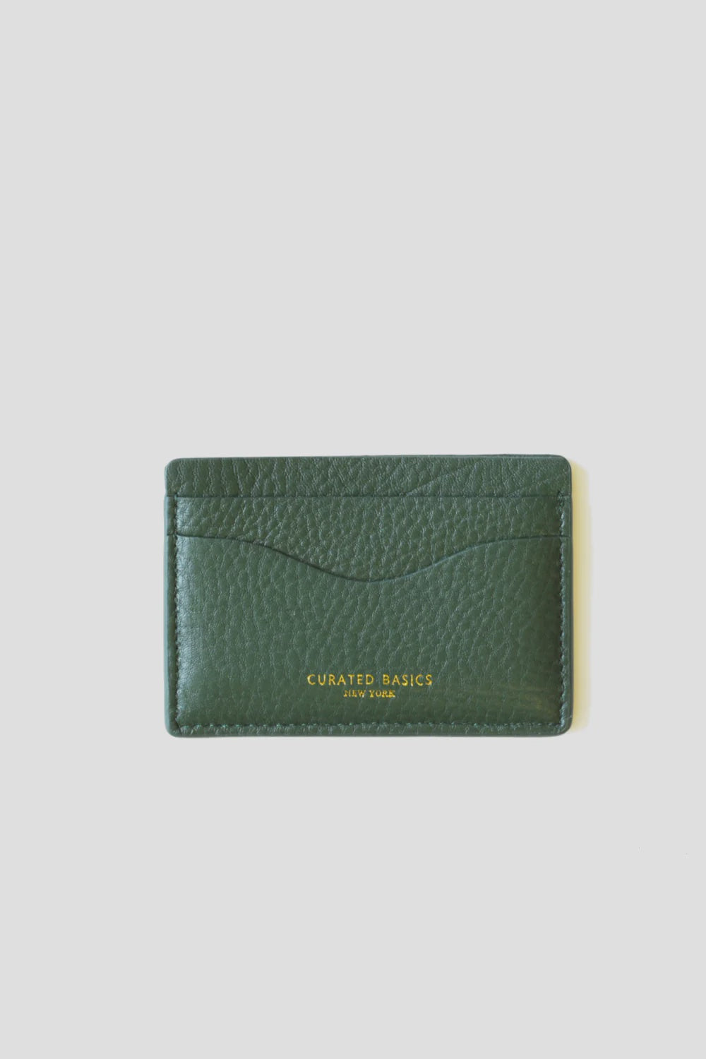 A textured lambskin leather cardholder in green features two slots, with "Curated Basics" gold lettering at the bottom. The MENS Leather Cardholder by Curated Basics is positioned against a plain white background, highlighting its elegant design.