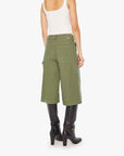 A woman is seen from the back wearing Mother’s The Half Chisel army green high-waisted capris with utility patch pockets, a white tank top, and black heeled boots against a plain white background.