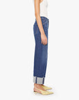 A person in a white sleeveless top and Mother’s Half Pipe Ankle high-waisted barrel jeans stands in profile, wearing yellow pointed-toe low-heel shoes against a plain white background.