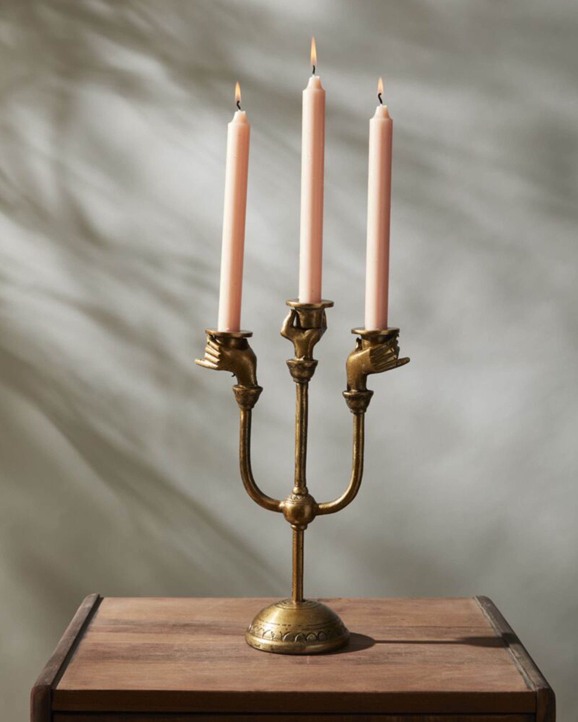 The Accent Decor Haunted Hands Candelabra features three glowing pink candles held by brass hands, making it a striking Halloween table decor piece on a wooden surface against a softly lit, neutral background.