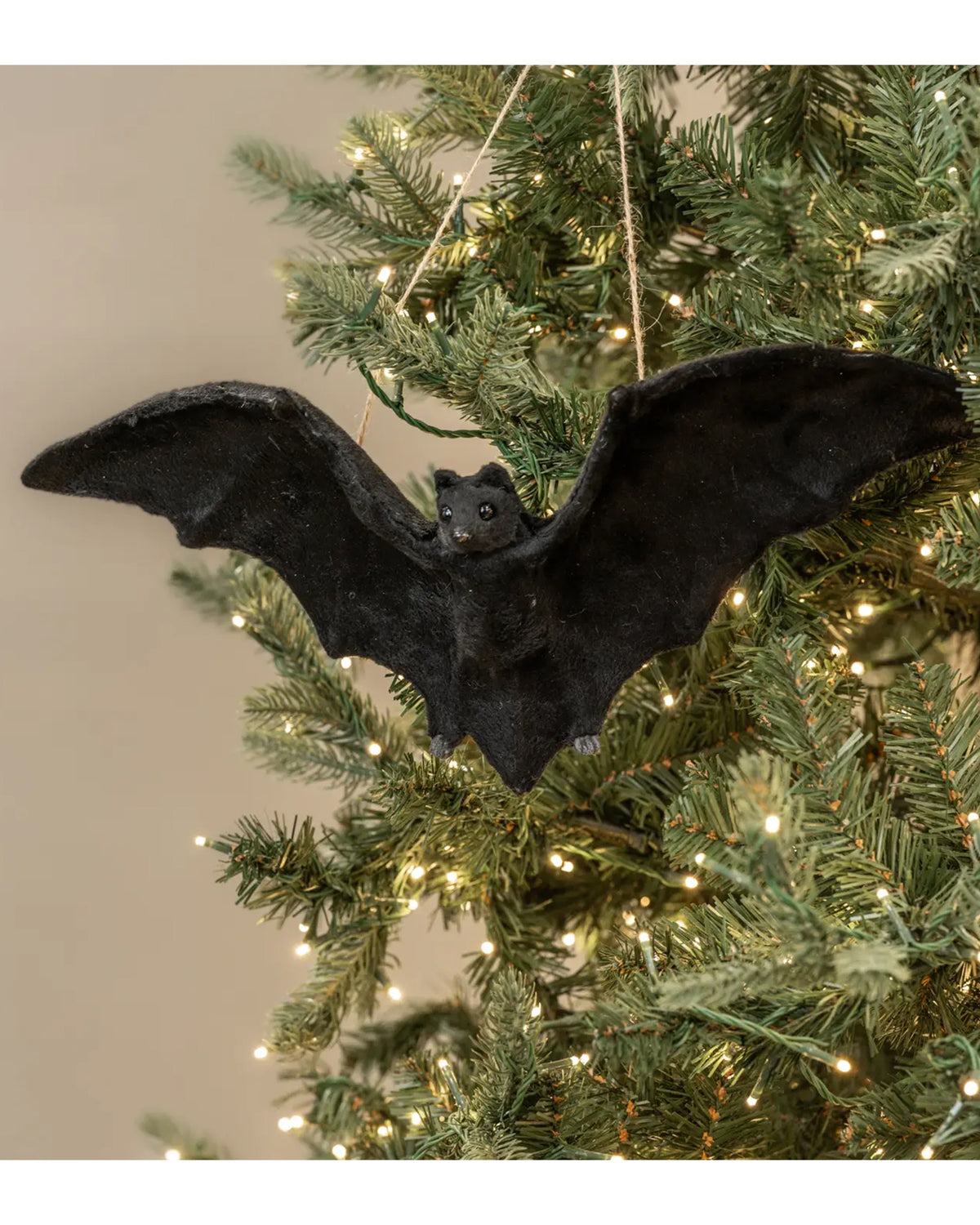 16.75″ Faire Bat Ornament on a lit Christmas tree, green branches in background, Bungalow Furniture &amp; Accessories.