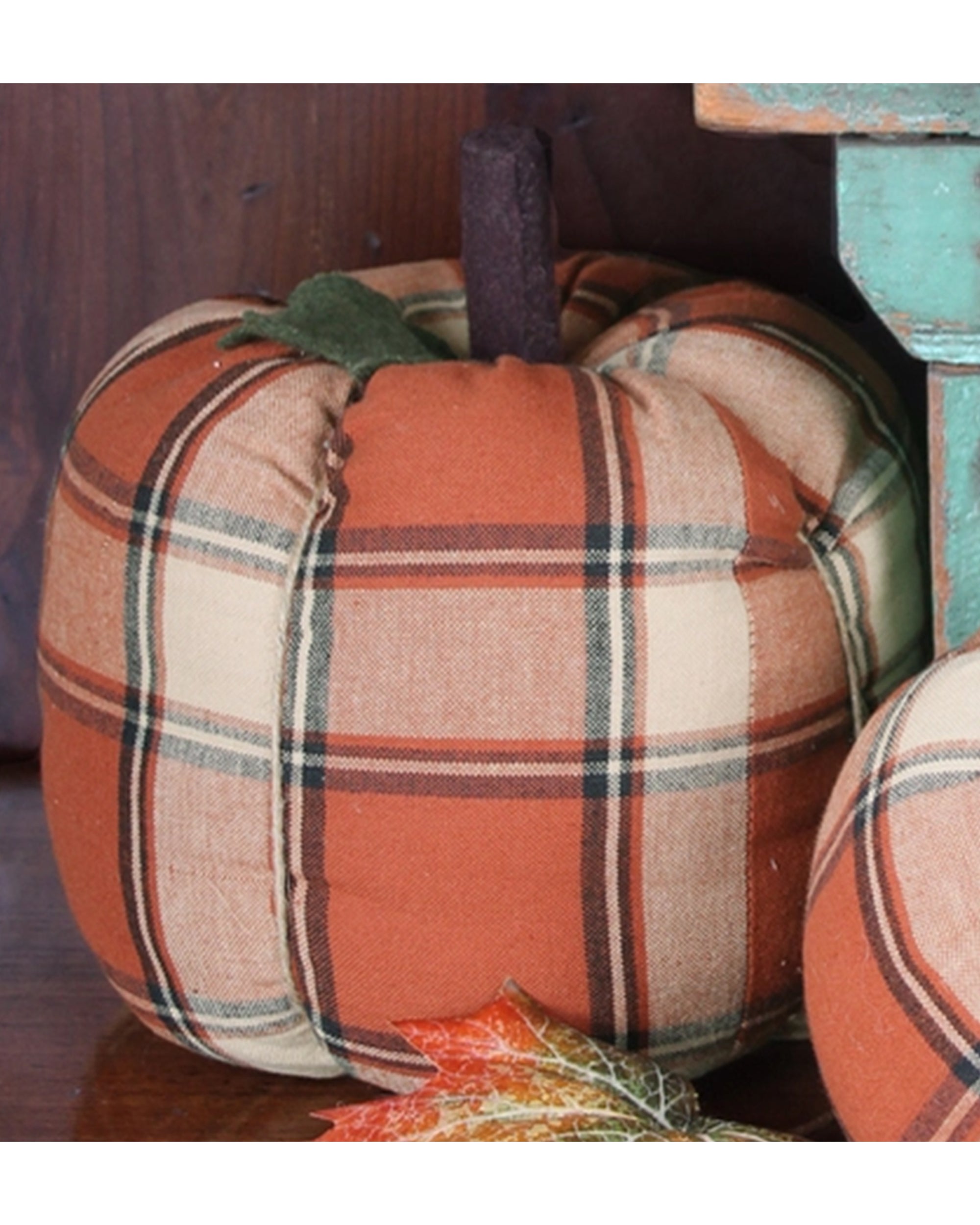 The Faire Pumpkin features a cozy orange, cream, and brown plaid fabric with a brown stem and green fabric leaf, making it ideal farmhouse decor or a charming fall ornament for your home.