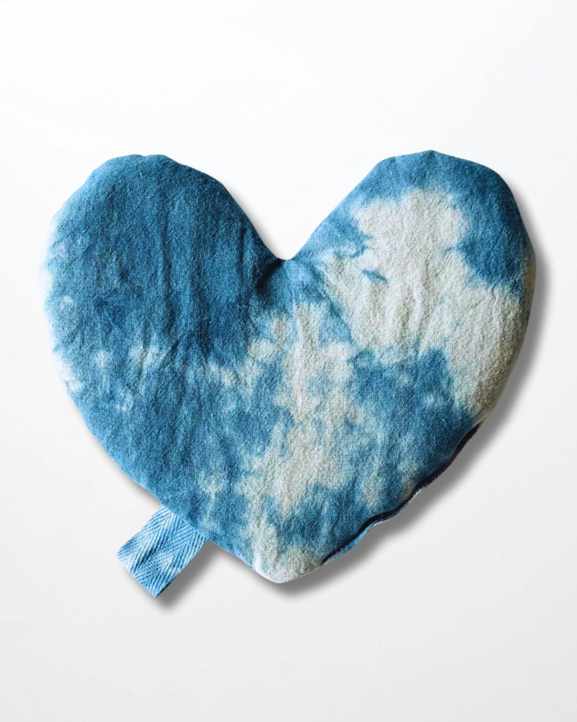 The Faire Heart Eye Pillow is a heart-shaped cotton eye pillow with a blue and white tie-dye pattern and a small blue fabric loop at the bottom, shown against a plain white background.