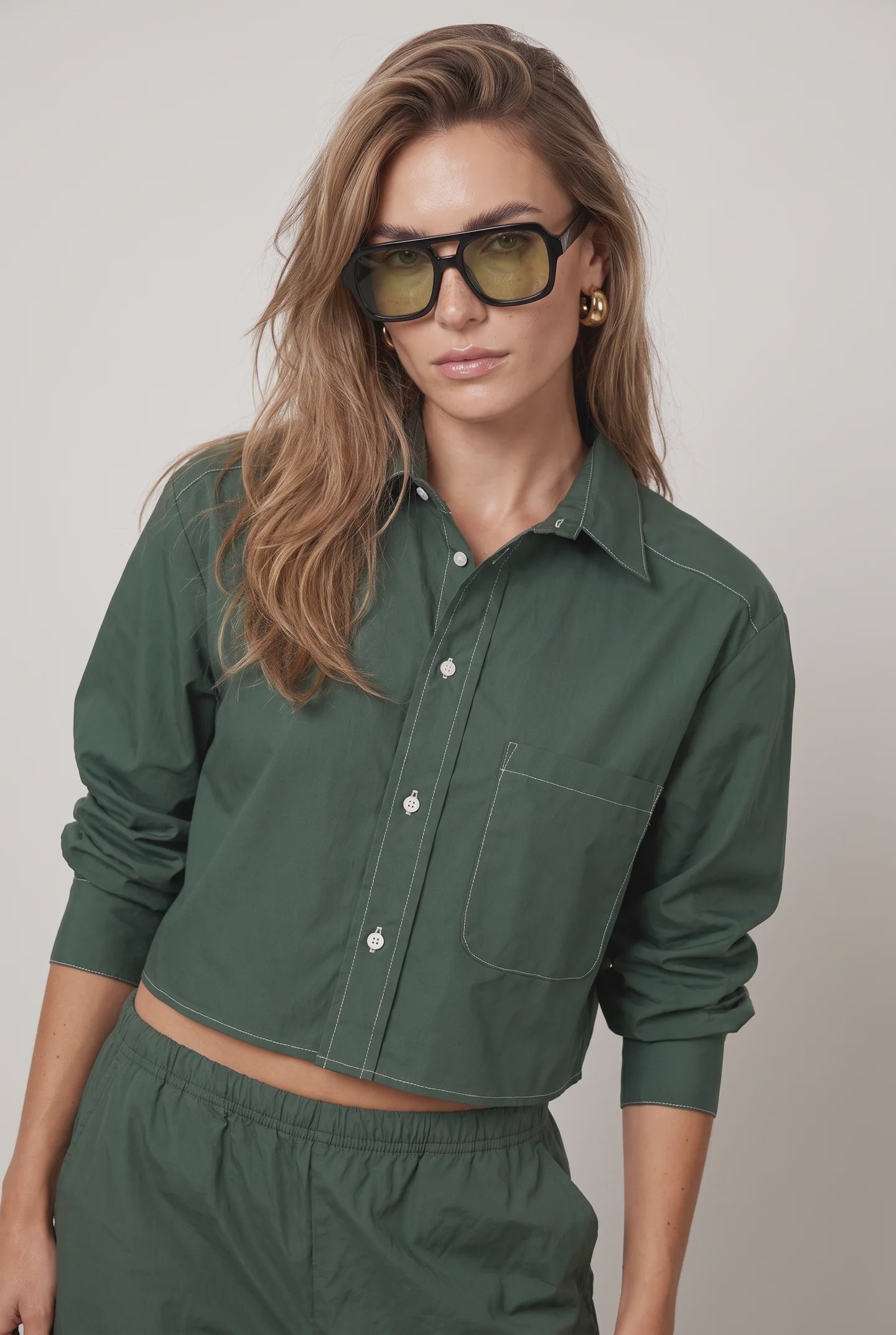 Olive-green sunglasses paired with THE SHIRT’s white-stitched Harper shirt and matching pants, modern casual style.