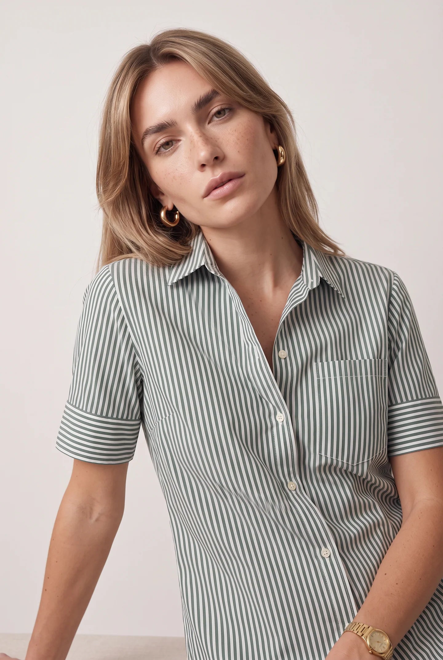 Short sleeve Hunter Stripe shirt by THE SHIRT, gold hoop earrings, and watch styled on woman looking at camera.