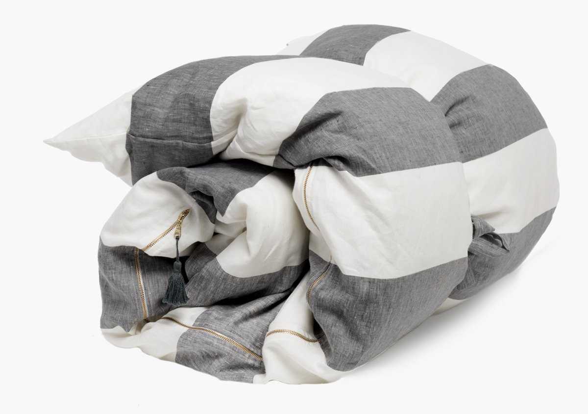 The Hedgehouse Throwbed features wide horizontal gray and white stripes, a small green tassel on one seam, and a removable cotton cover for easy care.