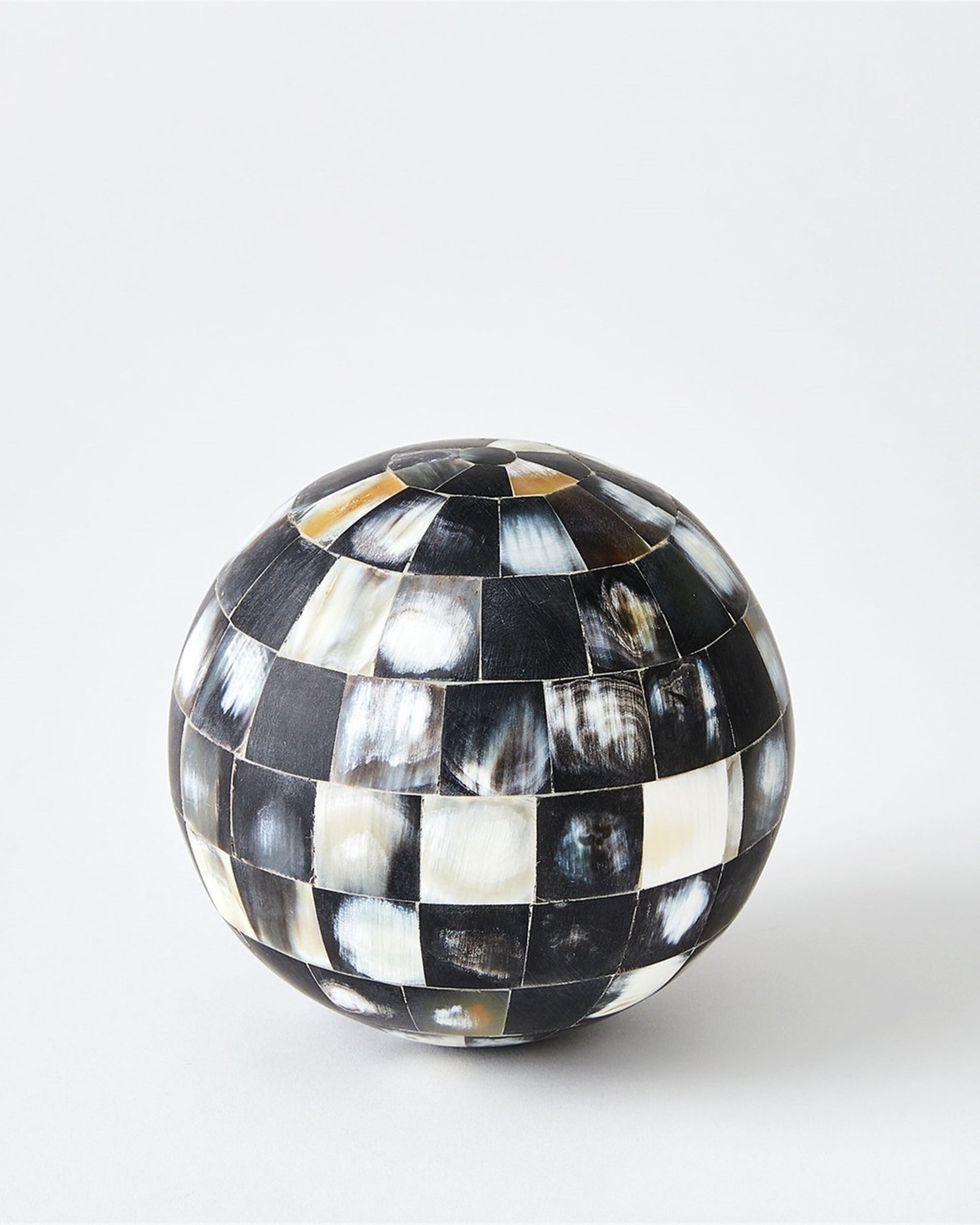 The 9.93948 Horn Sphere M by Global Views features a checkered mosaic of black, white, and gray tiles on a plain backdrop—a striking accent for luxury home decor.