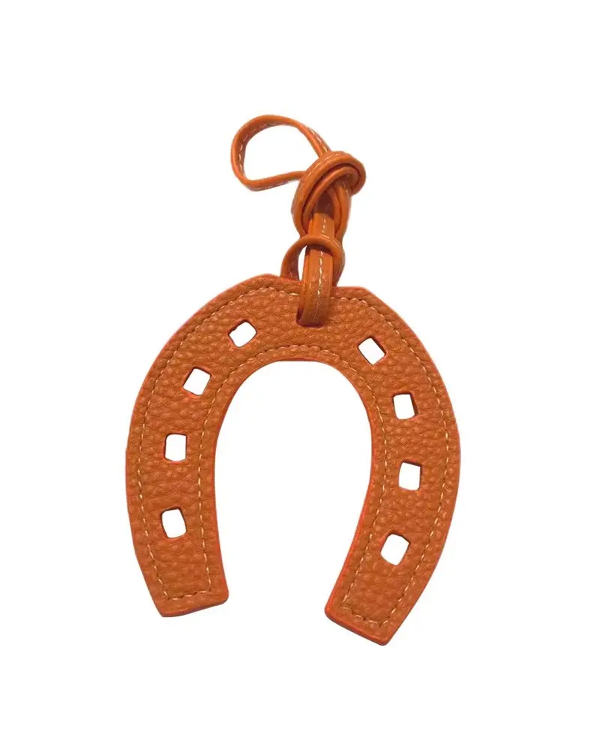 The Faire Bag Charm is a textured orange leather, horseshoe-shaped accessory with square cutouts and a matching hanging loop, adding a stylish, personal touch. Displayed on a white background.