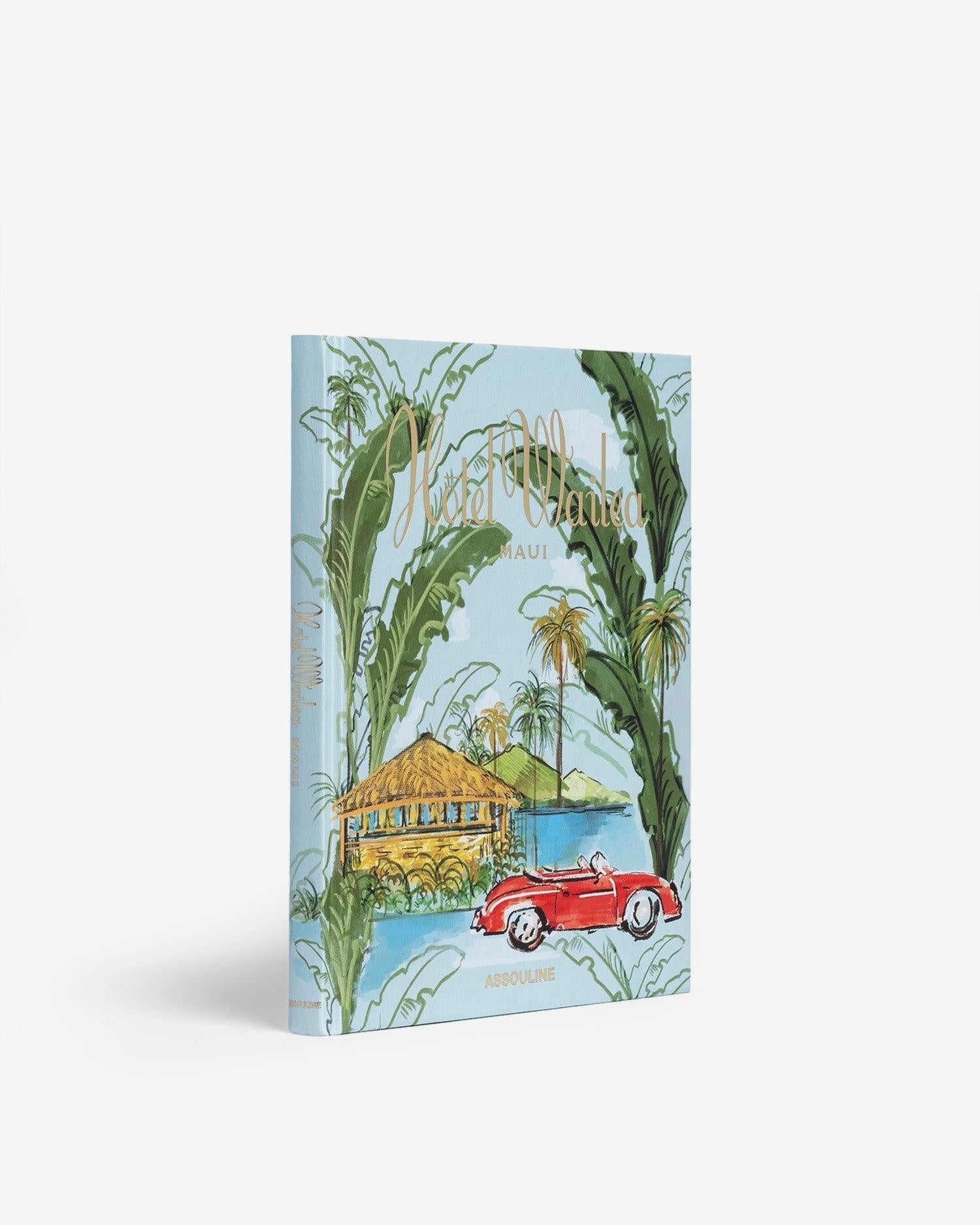 A book titled "Hotel Wailea" by Assouline, featuring an illustration of a Maui boutique resort with a thatched roof surrounded by palm trees. A red convertible car is parked in the foreground. The cover has a light blue background with green tropical leaves framing the image, evoking a Hawaiian-island escape.