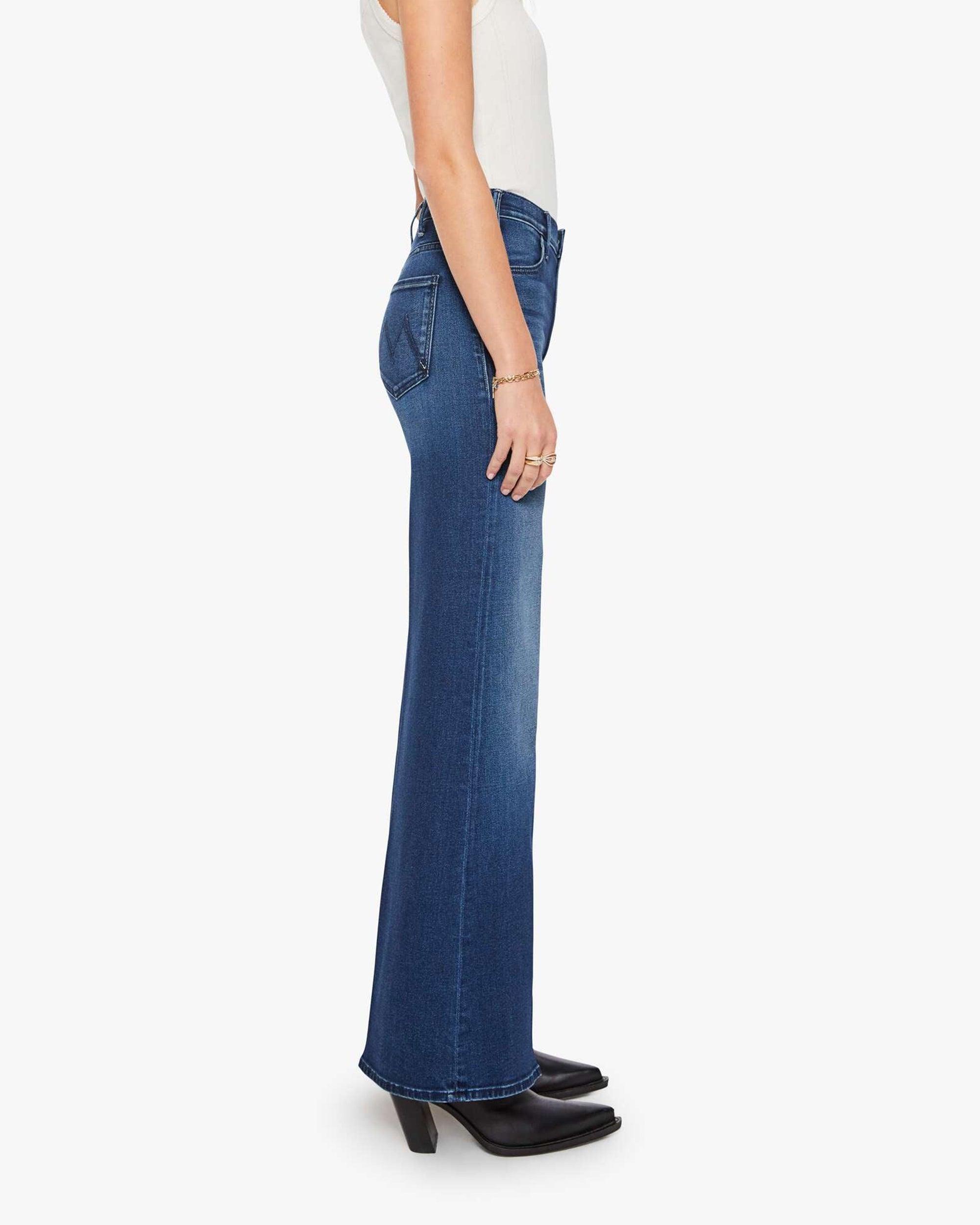 Mother’s The Hustler Roller Sneak blue jeans styled with a white top and black boots, shown in profile.