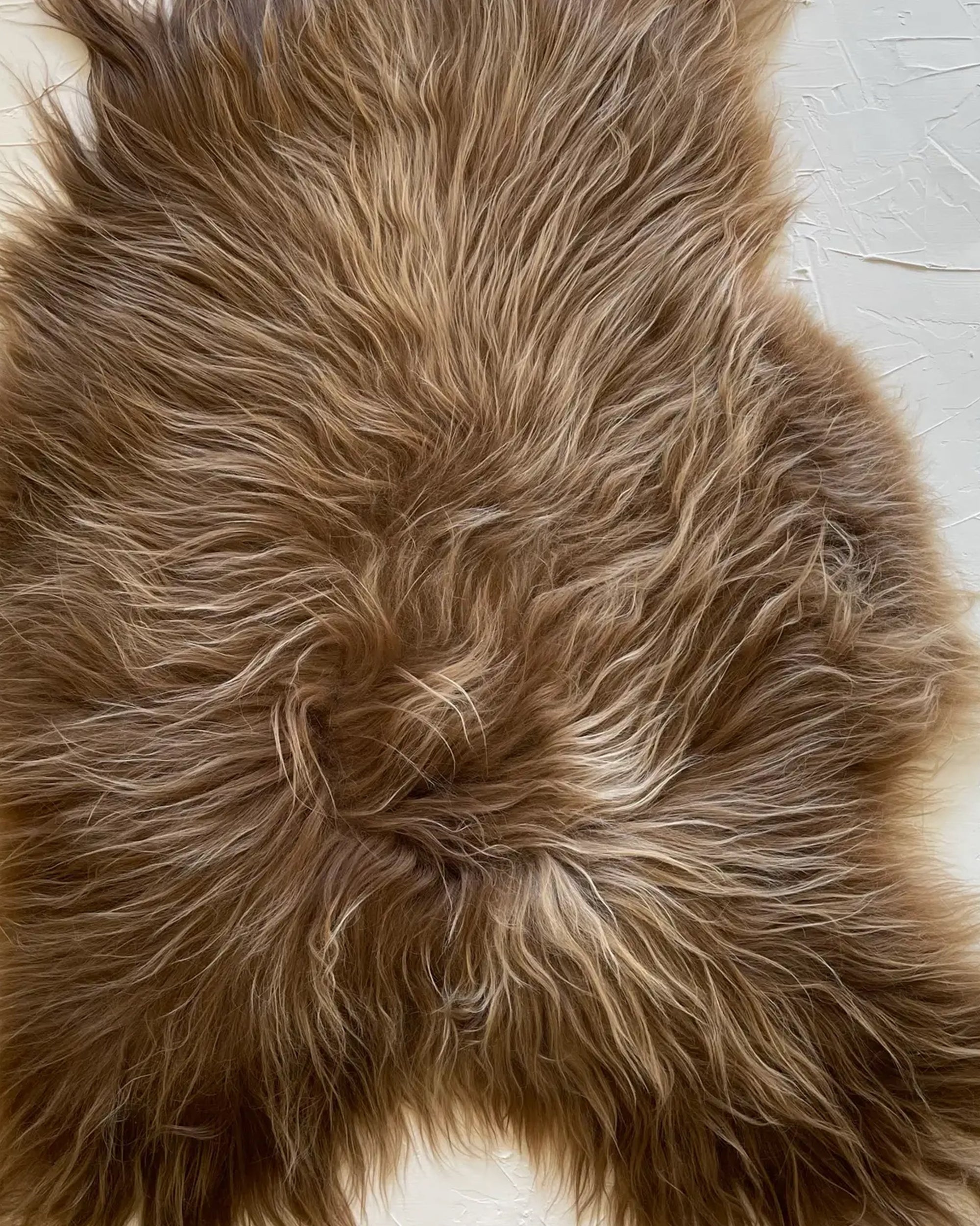 A close-up of the Faire Icelandic Sheepskin rug showcases its long, fluffy, wavy hair spread across a light textured surface.