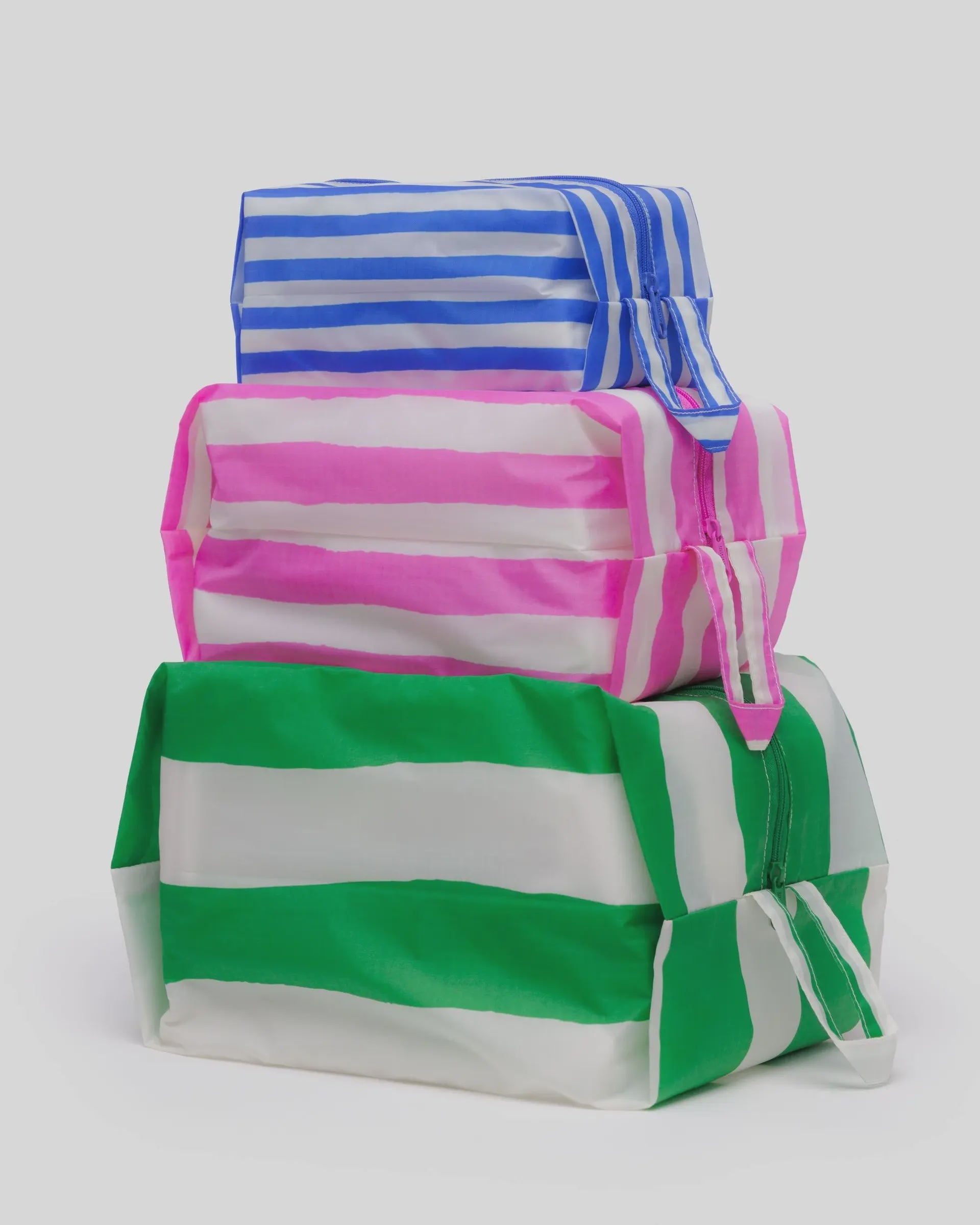 The Baggu 3D Zip Set includes three rectangular pouches—blue, pink, and green—with horizontal stripes, made from recycled nylon. Each features a zip closure and small handle, ideal for keeping your essentials organized while traveling.