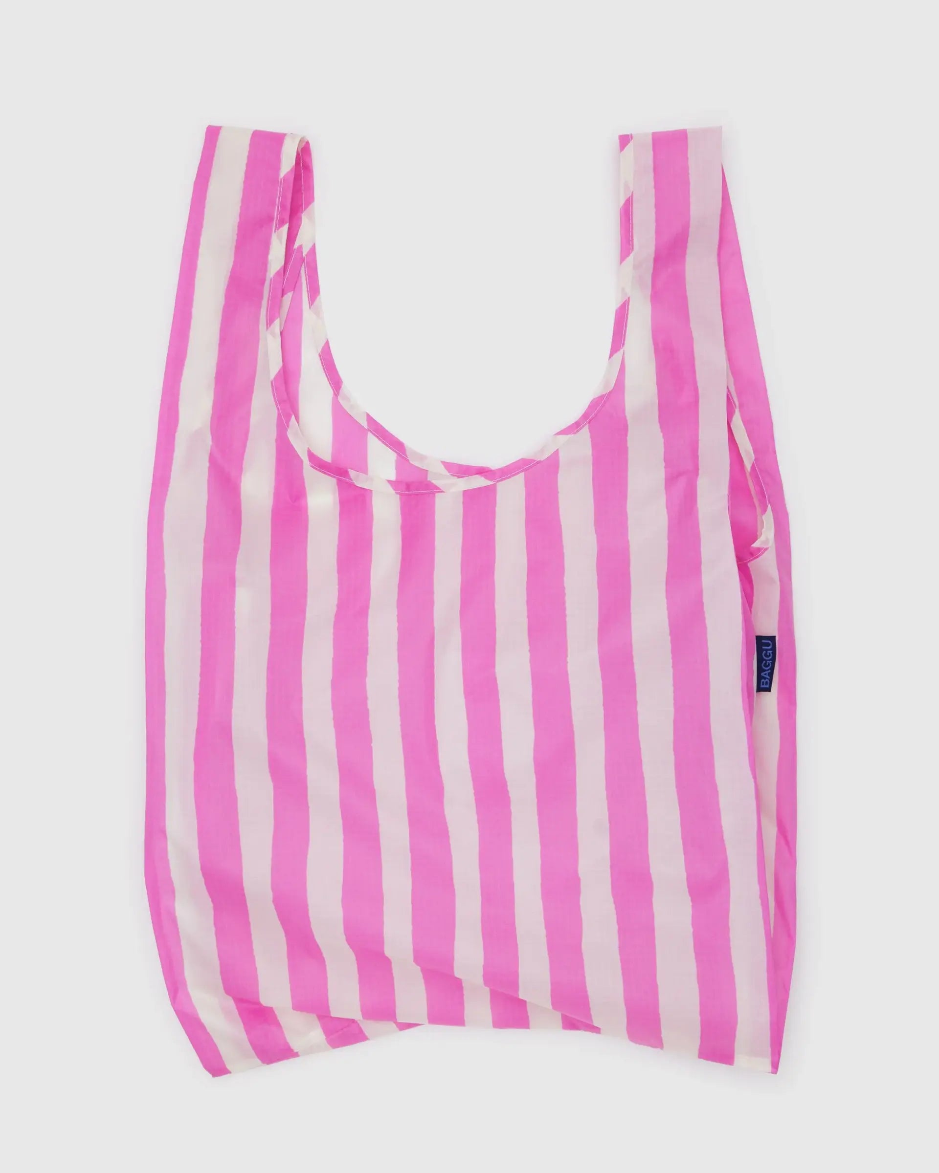 The Baggu Standard by Baggu is a rectangular, reusable bag made from recycled ripstop nylon with vertical pink and white stripes. It has wide handles, is machine washable, and is shown laying flat against a white background.