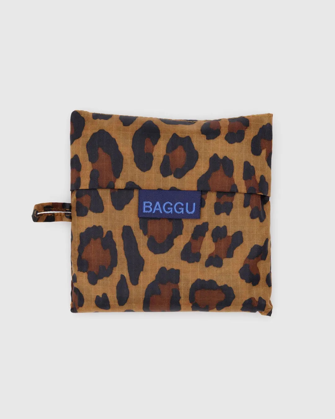 The Baggu Standard is a leopard print, foldable reusable bag made from recycled ripstop nylon with a handle loop. It features a bold blue Baggu label on the front and is eco-friendly, machine washable, and shown against a white background.