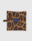 The Baggu Standard is a leopard print, foldable reusable bag made from recycled ripstop nylon with a handle loop. It features a bold blue Baggu label on the front and is eco-friendly, machine washable, and shown against a white background.