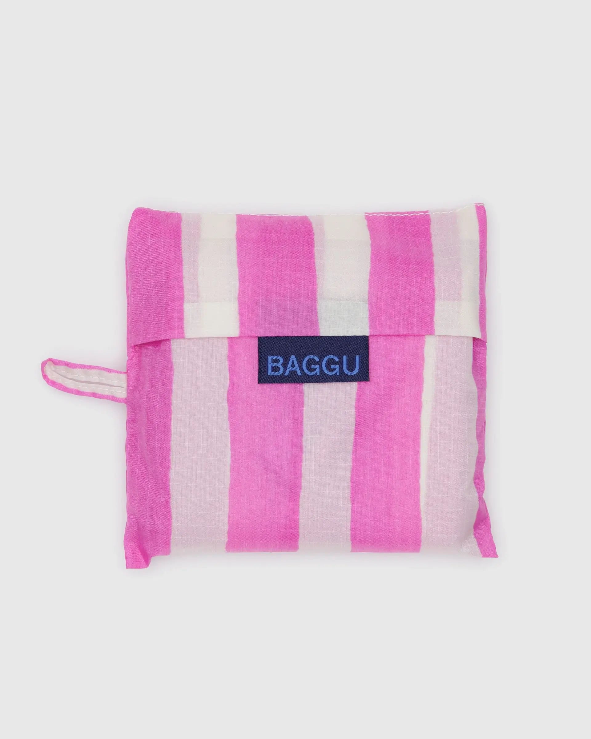 The Baggu Standard by Baggu, a folded reusable bag with vertical pink and white stripes made from recycled ripstop nylon, features a blue Baggu label on the front and is shown against a plain light background.