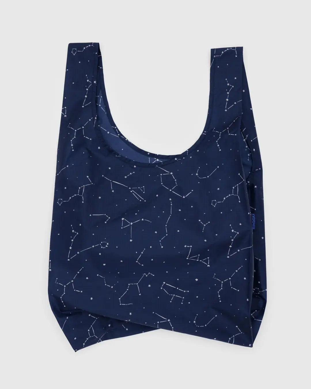 The Baggu Standard by Baggu is a reusable, dark blue shopping bag made from recycled ripstop nylon and adorned with a white constellation pattern. It features a simple design, handle for easy carrying, and is machine washable.