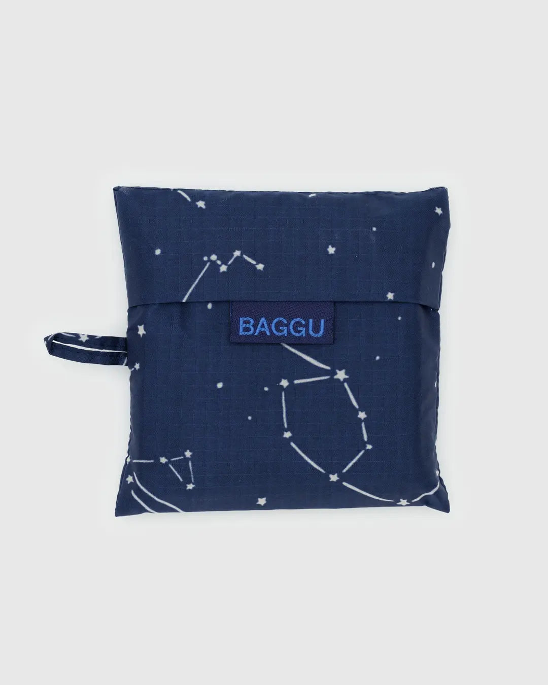 The Baggu Standard is a square pouch in dark blue, made from recycled ripstop nylon featuring a constellation design and side handle. "BAGGU" is printed on the center flap in blue. This reusable, machine-washable bag is displayed against a light gray background for easy care.