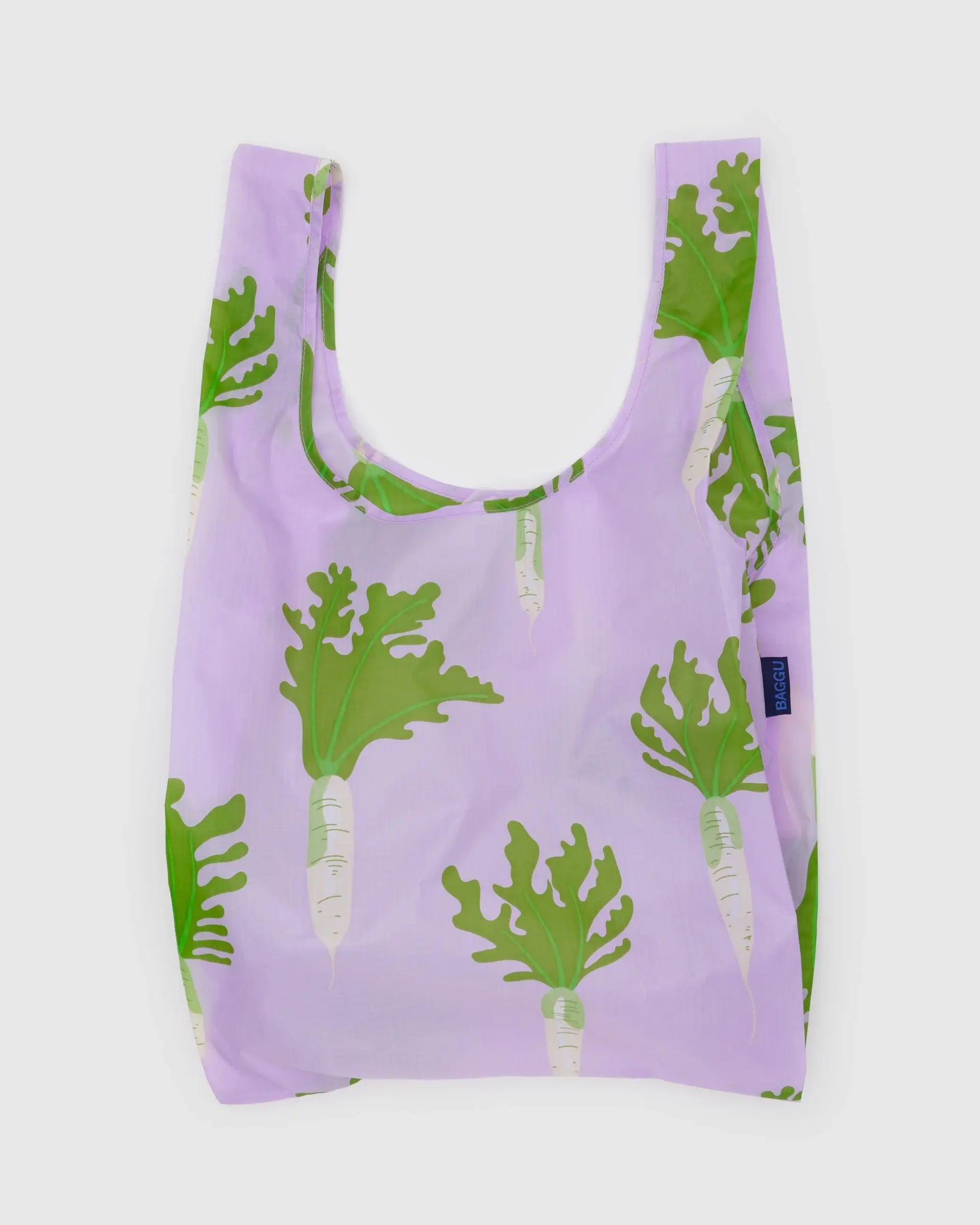The Baggu Standard by Baggu is a reusable bag made from recycled ripstop nylon, with a light purple background and green daikon radish print. It features wide handles, a soft rectangular shape, and is machine washable for easy care.