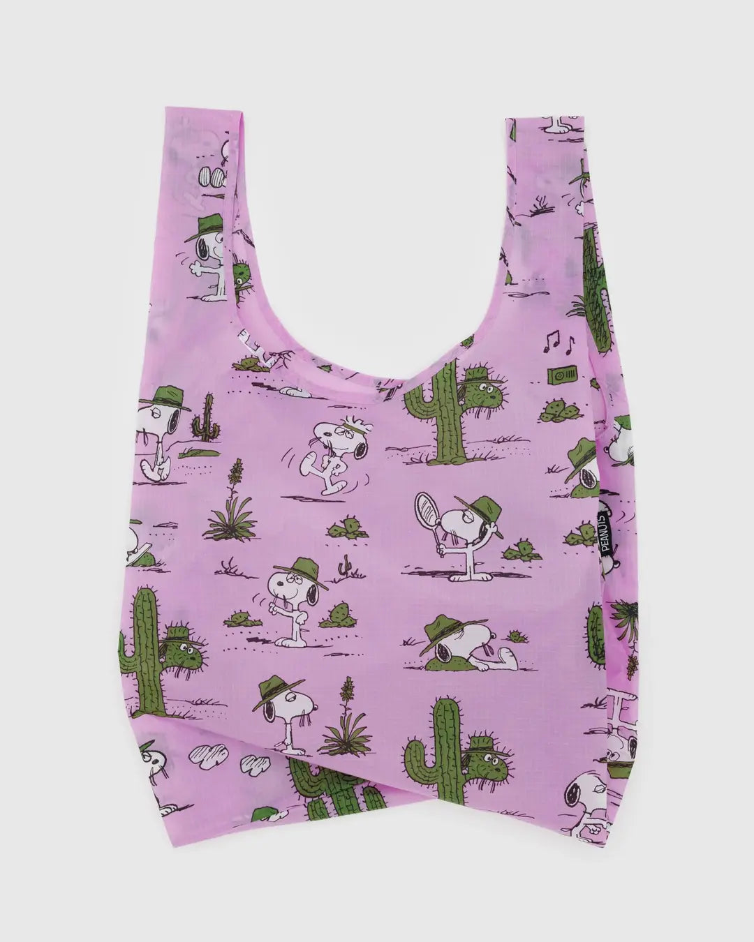 The Baggu Standard by Baggu is a pink reusable bag crafted from recycled ripstop nylon, featuring cartoon drawings of a white dog wearing a green hat. The design includes the pup enjoying tennis and photography amid whimsical cacti and musical notes. It's also machine washable for easy care!.