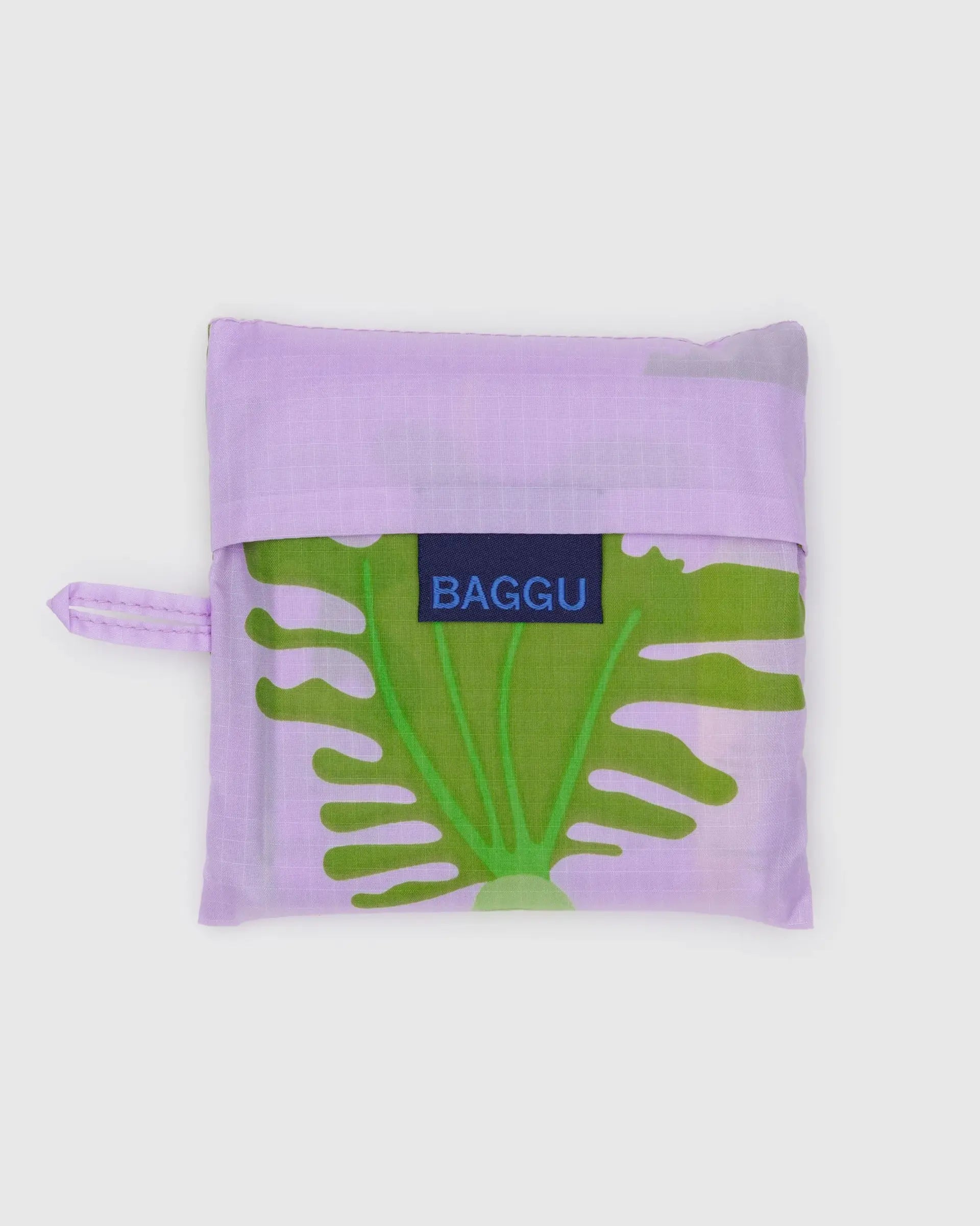 The Baggu Standard by Baggu is a folded reusable bag in a lavender pouch, made from recycled ripstop nylon with a green botanical print partly visible and a blue BAGGU label on the front. It&#39;s machine washable for easy care.