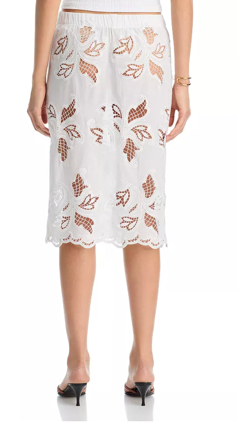 A woman wears the Cissa Summer Pencil Skirt—a white pull-on midi skirt with embroidered floral cutouts—paired with black heeled sandals and a gold bracelet, standing with her back to the camera.