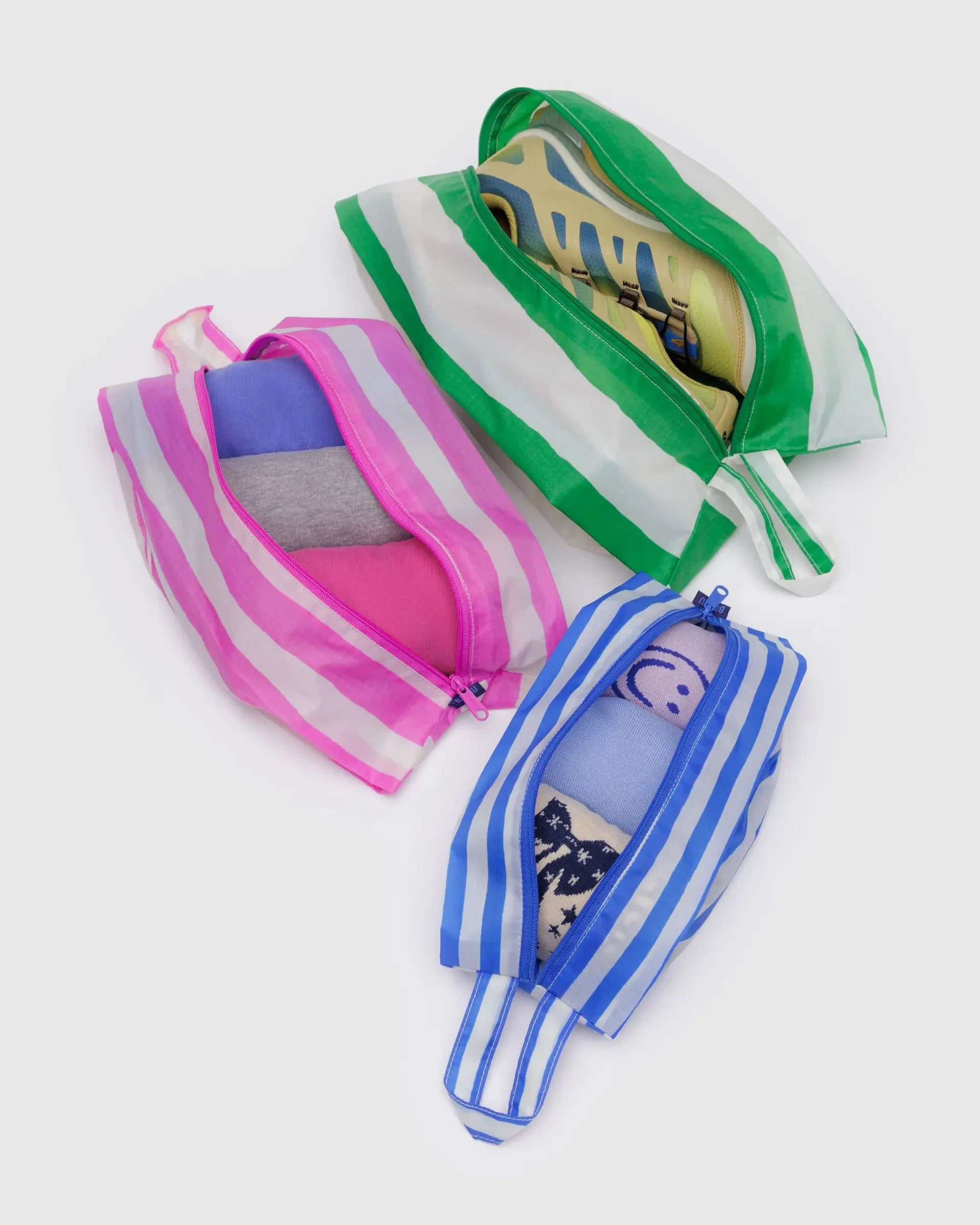The Baggu 3D Zip Set features three striped zippered pouches in green, pink, and blue—ideal for organizing shoes, clothes, and accessories while traveling. Stylishly arranged on a light background for a chic look.