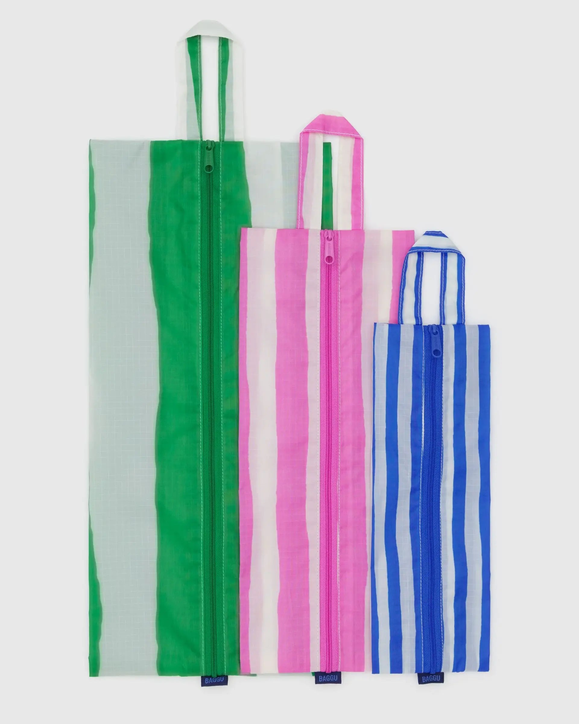 The Baggu 3D Zip Set features three recycled nylon pouches in green/white, pink/white, and blue/white bold stripes. Each pouch stands upright, has a handle, and offers stylish organization for travel or everyday use.