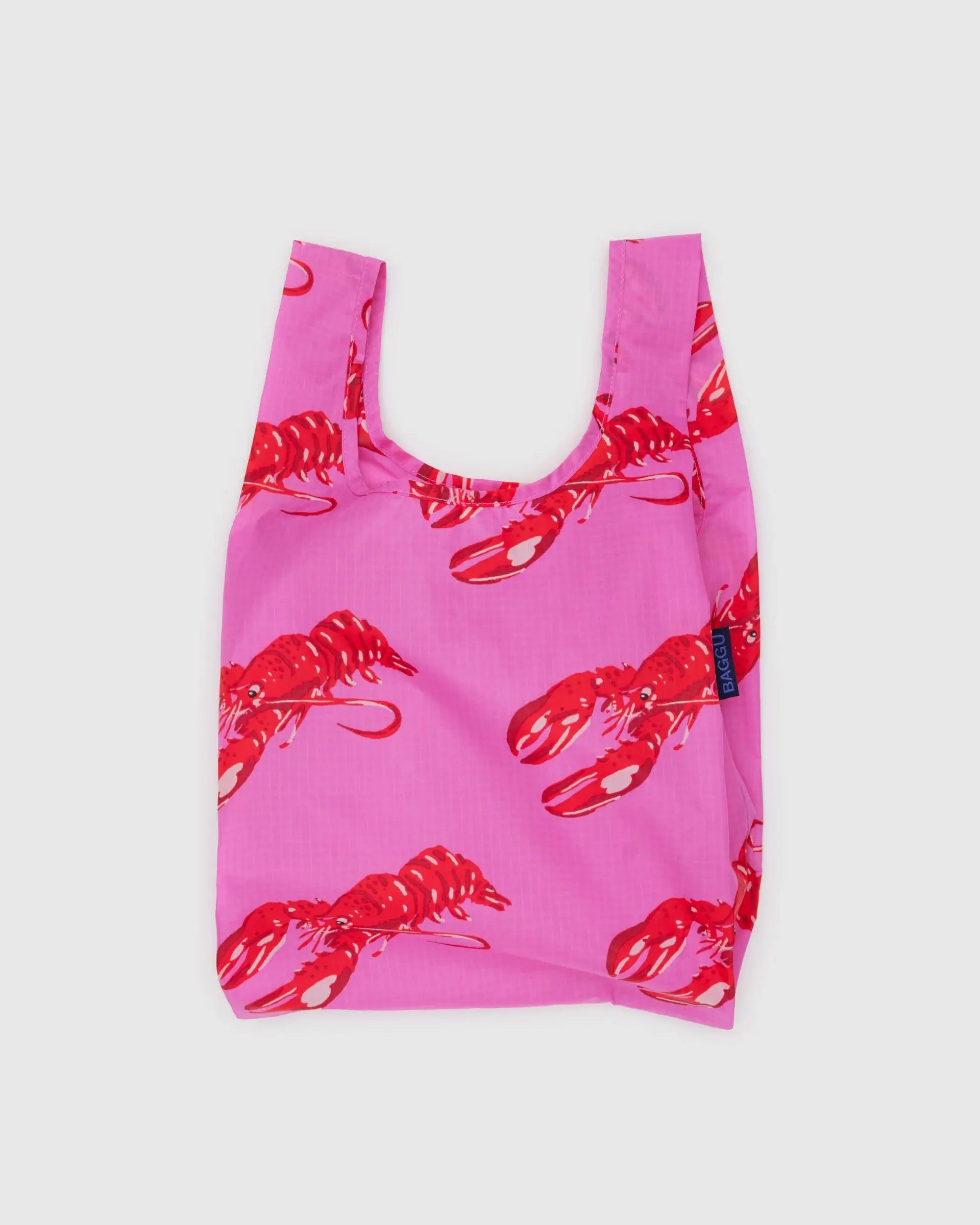 The Baby Baggu by Baggu is a pink reusable shopping bag made from recycled ripstop nylon, featuring red lobster prints. It is shown against a simple light background.