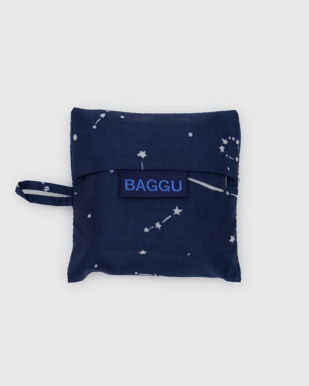 The Baby Baggu reusable shopping bag in navy blue with a white constellation pattern is made from recycled ripstop nylon, featuring a small handle loop and a blue tag with "BAGGU." It’s also machine washable.