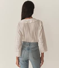 A person with long dark hair wears the Huguette Top by DOEN with lace sleeves and high-waisted blue jeans, standing with their back to the camera against a plain background.