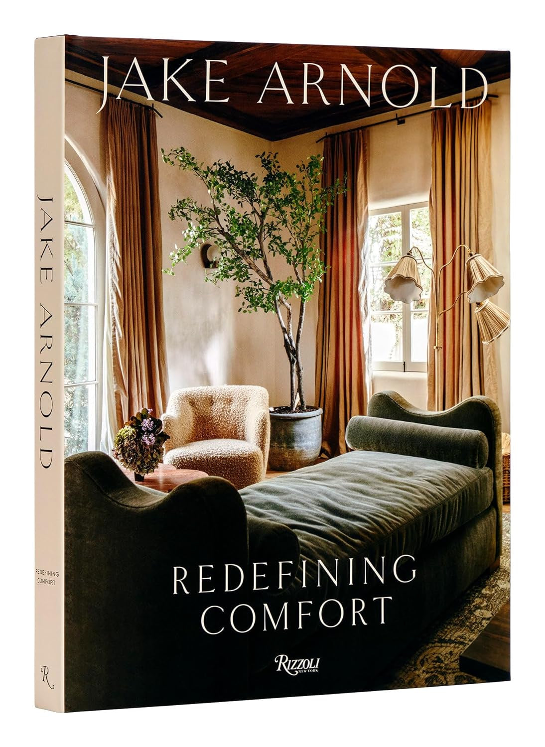 The book cover for "Redefining Comfort: Jake Arnold" by Random House shows a modern living room with neutral furniture, a potted tree, and large windows letting in plenty of light. The Random House logo is displayed at the bottom.