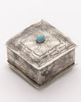 The Small Stamped Box w/ Turquoise by J Alexander Rustic Silver features engraved patterns and a central turquoise stone on the lid, shown angled on a white background—ideal as a Turquoise Treasure Box for Southwestern decor.