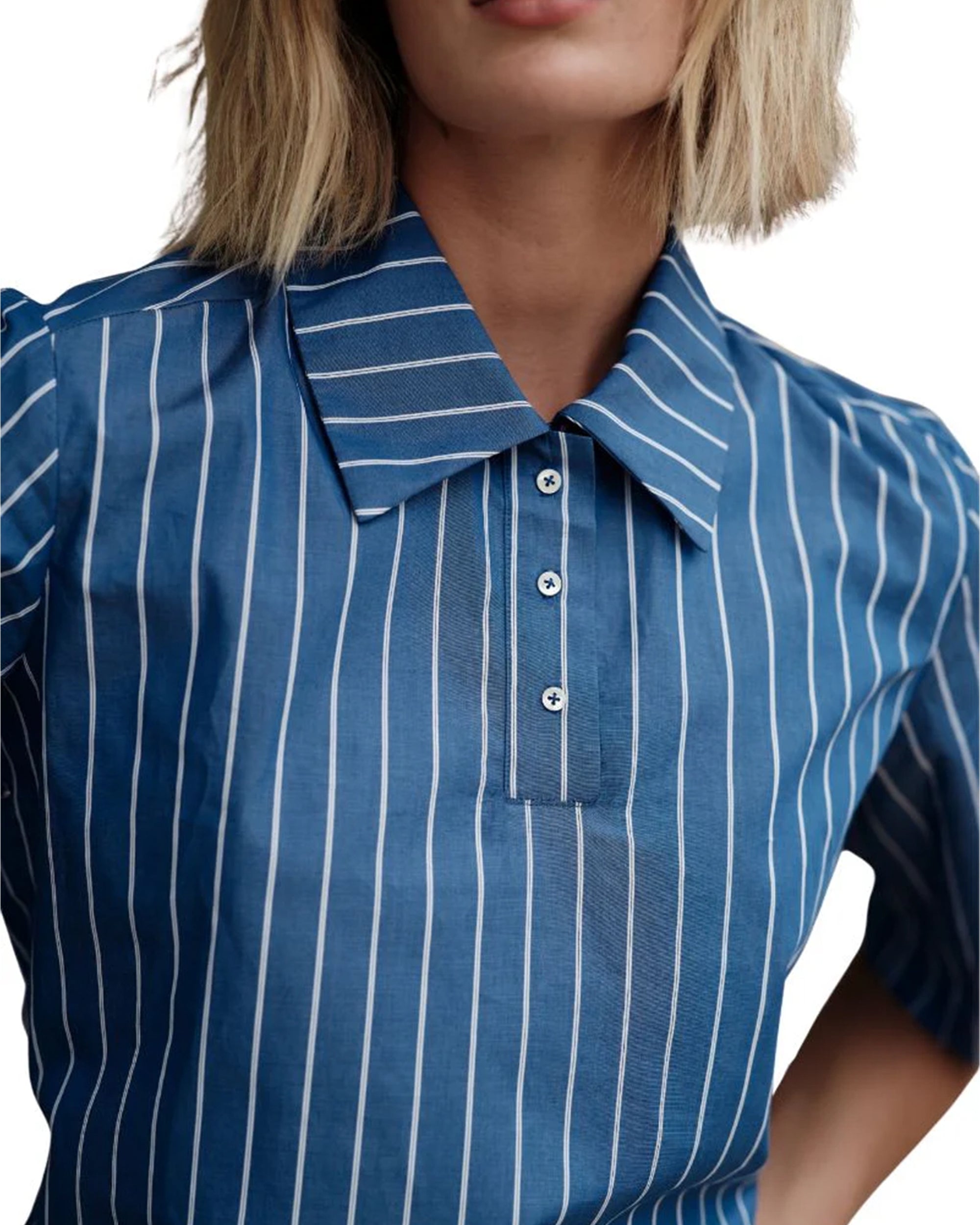 A person with blonde hair wears The Polo Shirt by Cissa, a blue collared top with white Keswick stripes and a partial button placket. The image is cropped to show only the head and upper torso.