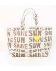 The KR Sunshine Tote by Kerri Rosenthal is a white cotton canvas bag featuring bold brown "SUN SHINE" text, Kerri's signature artwork, two handles, and a yellow heart-shaped charm for a cheerful touch.