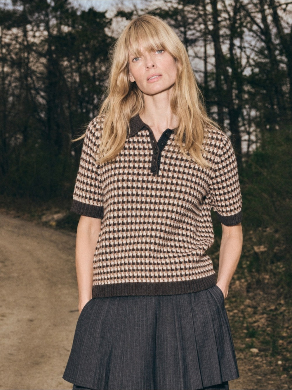Sea New York DECLAN short sleeve polo sweater in light color, styled with a dark skirt on a wooded path.