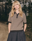 Sea New York DECLAN short sleeve polo sweater in light color, styled with a dark skirt on a wooded path.
