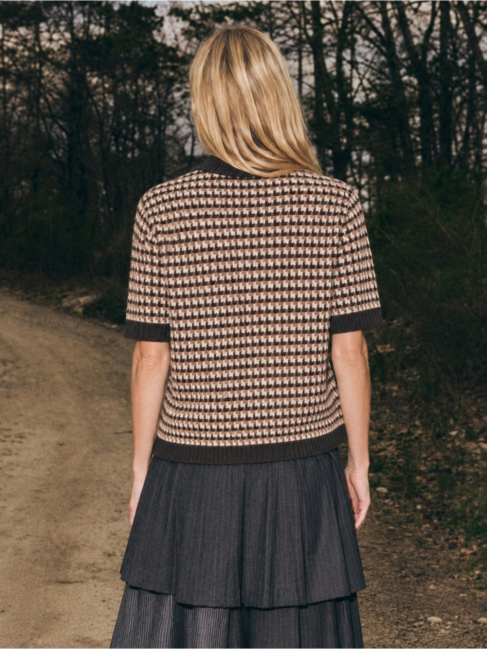 Sea New York DECLAN short sleeve polo sweater and pleated skirt in a relaxed, outdoor setting on a dirt road.