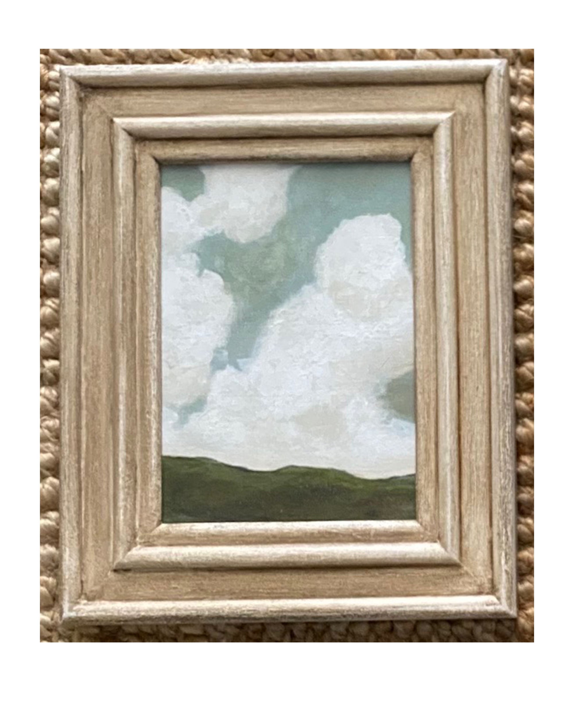 The Tak Design LANDSCAPES Framed Art features green hills and a blue sky with white clouds in a rustic light wood frame, making this hand-painted piece a charming home decor accent for any textured beige surface.