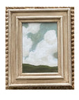 The Tak Design LANDSCAPES Framed Art features green hills and a blue sky with white clouds in a rustic light wood frame, making this hand-painted piece a charming home decor accent for any textured beige surface.