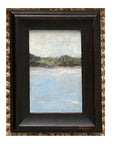 The Tak Design LANDSCAPES Framed Art features a peaceful scene with water, trees, a house, and a pale sky. Its dark vintage frame adds timeless charm, making it an ideal home decor piece.