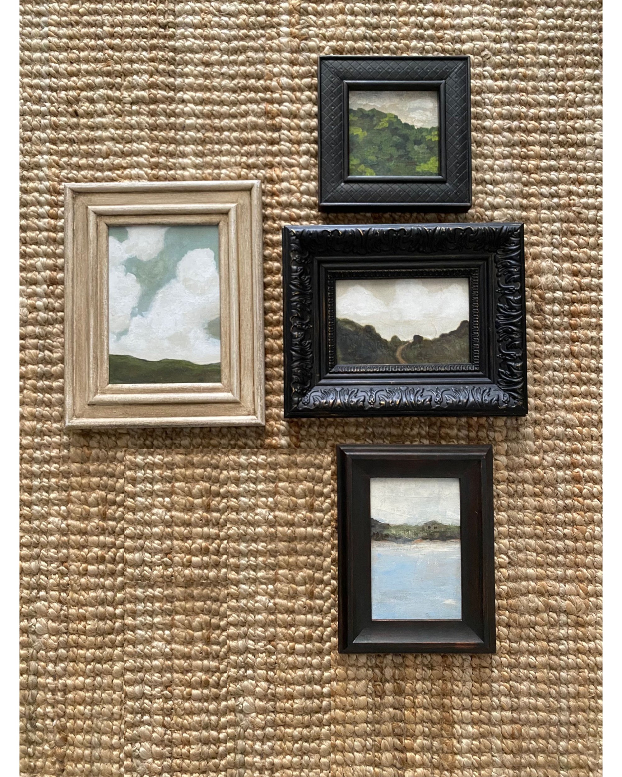 The LANDSCAPES Framed Art set by Tak Design features four small, hand-painted pieces in vintage frames arranged on a woven beige wall. Each artwork depicts clouds, hills, or water—an ideal touch of charm for any home decor.