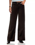 A person models LE Slim Palazzo Velvet women's wide-leg pants in dark brown with a black belt, styled with a light blue top and black heels. Only the lower half is shown against a crisp white background.