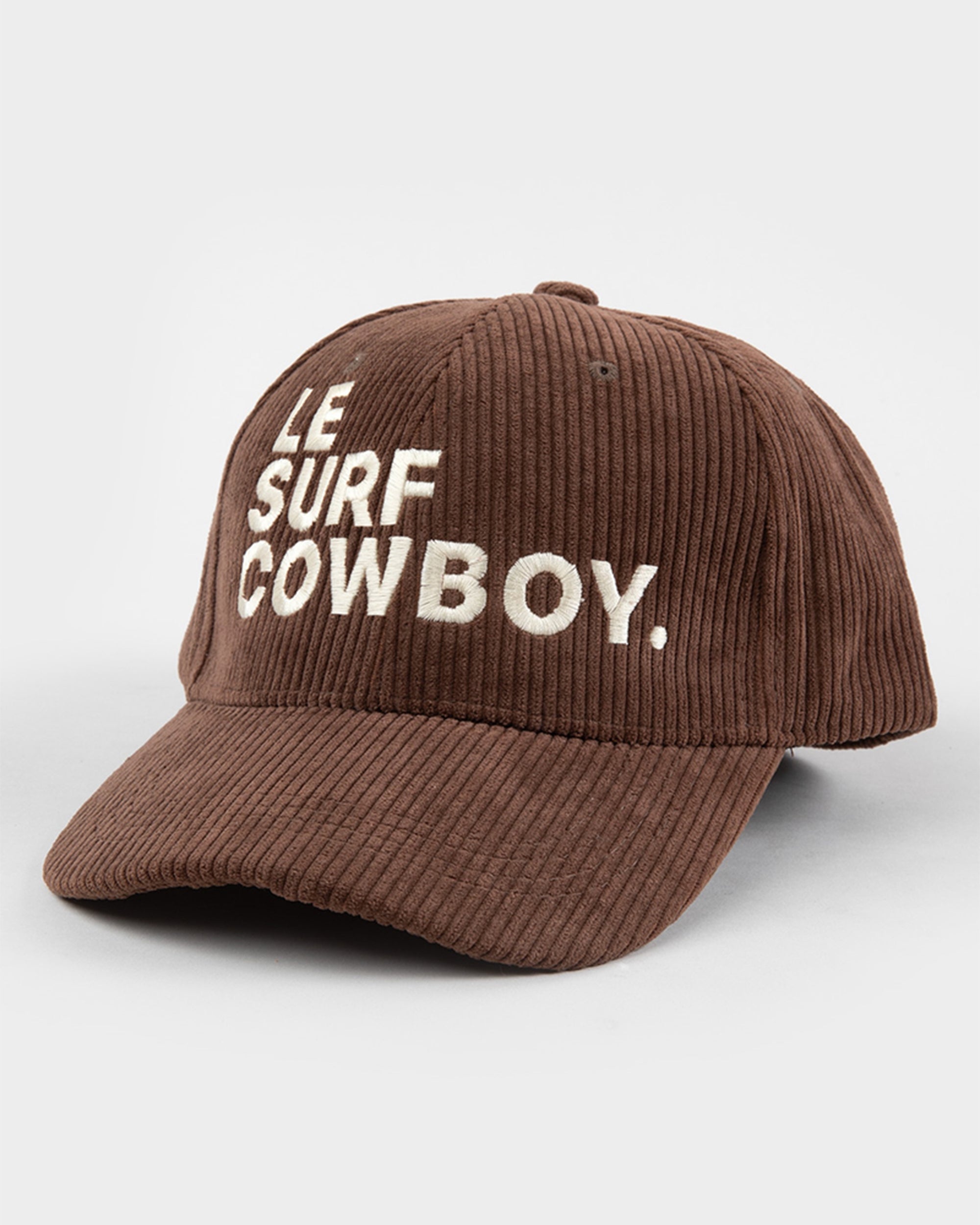 The Ping Pong Surf Club Le Surf Cowboy Corduroy Hat features brown corduroy, white "LE SURF COWBOY" embroidery on the front, and an adjustable strapback, blending style and comfort against a light background.