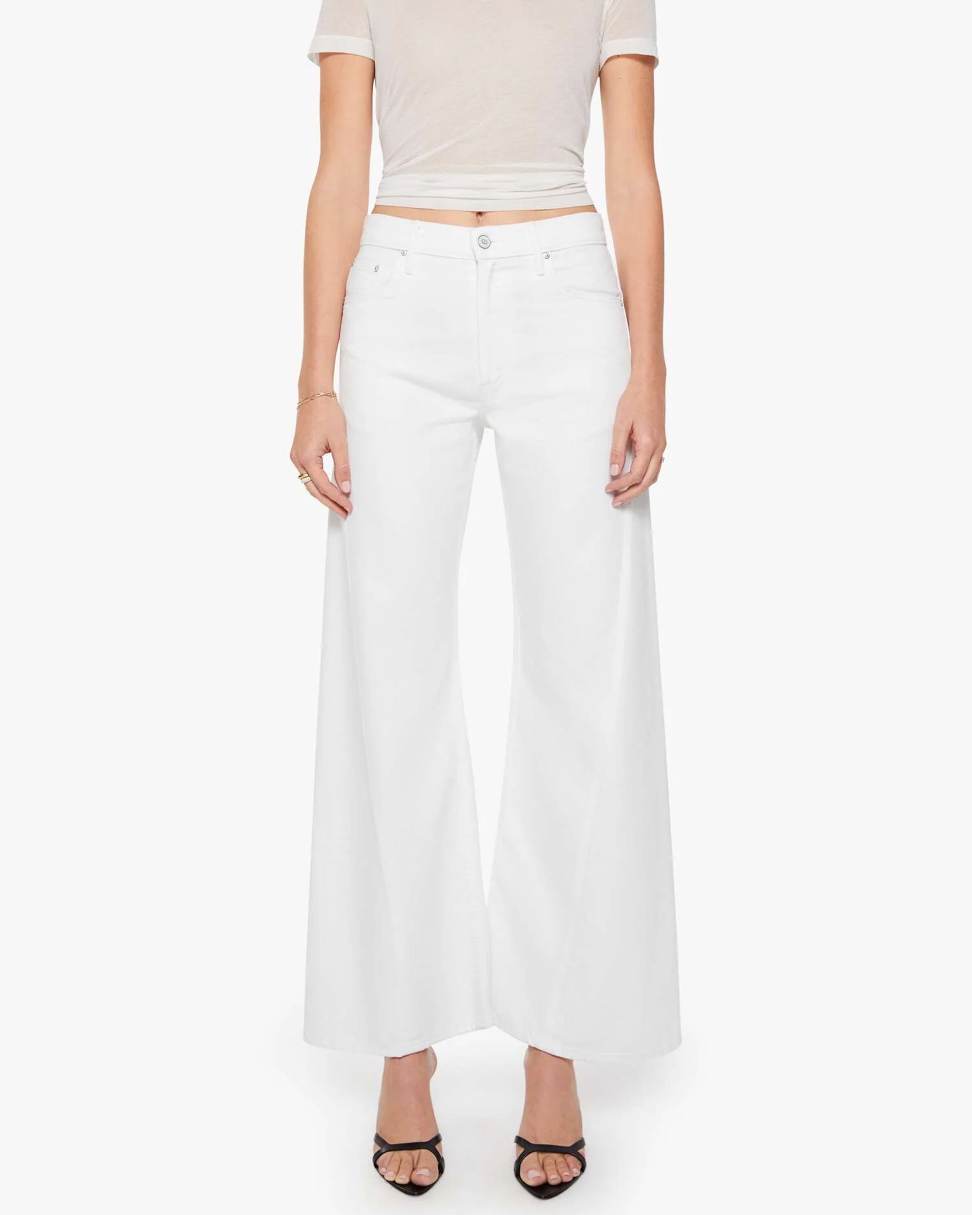 A person wears The Lemon Twist Skimp by Mother—high-rise, wide-leg cotton-blend pants—paired with a beige cropped top and black open-toe heels, standing against a white background.